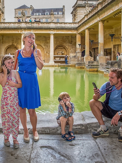 Tourists using audio guides at the Roman Baths in Bath, part of a day trip from London.