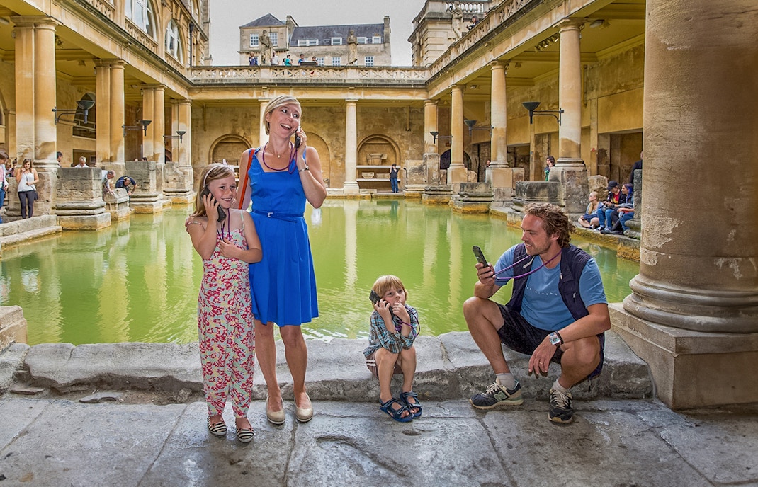 Tourists using audio guides at the Roman Baths in Bath, part of a day trip from London.
