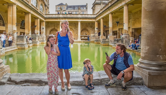 Tourists using audio guides at the Roman Baths in Bath, part of a day trip from London.