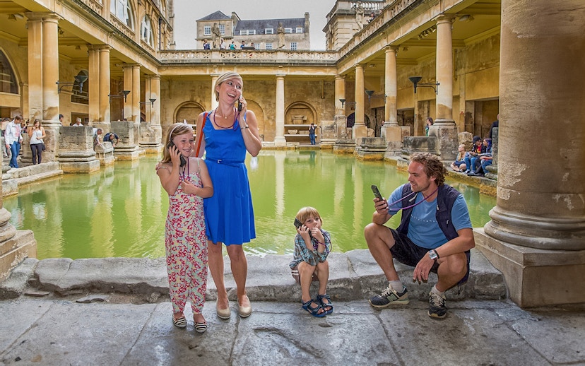 Tourists using audio guides at the Roman Baths in Bath, part of a day trip from London.