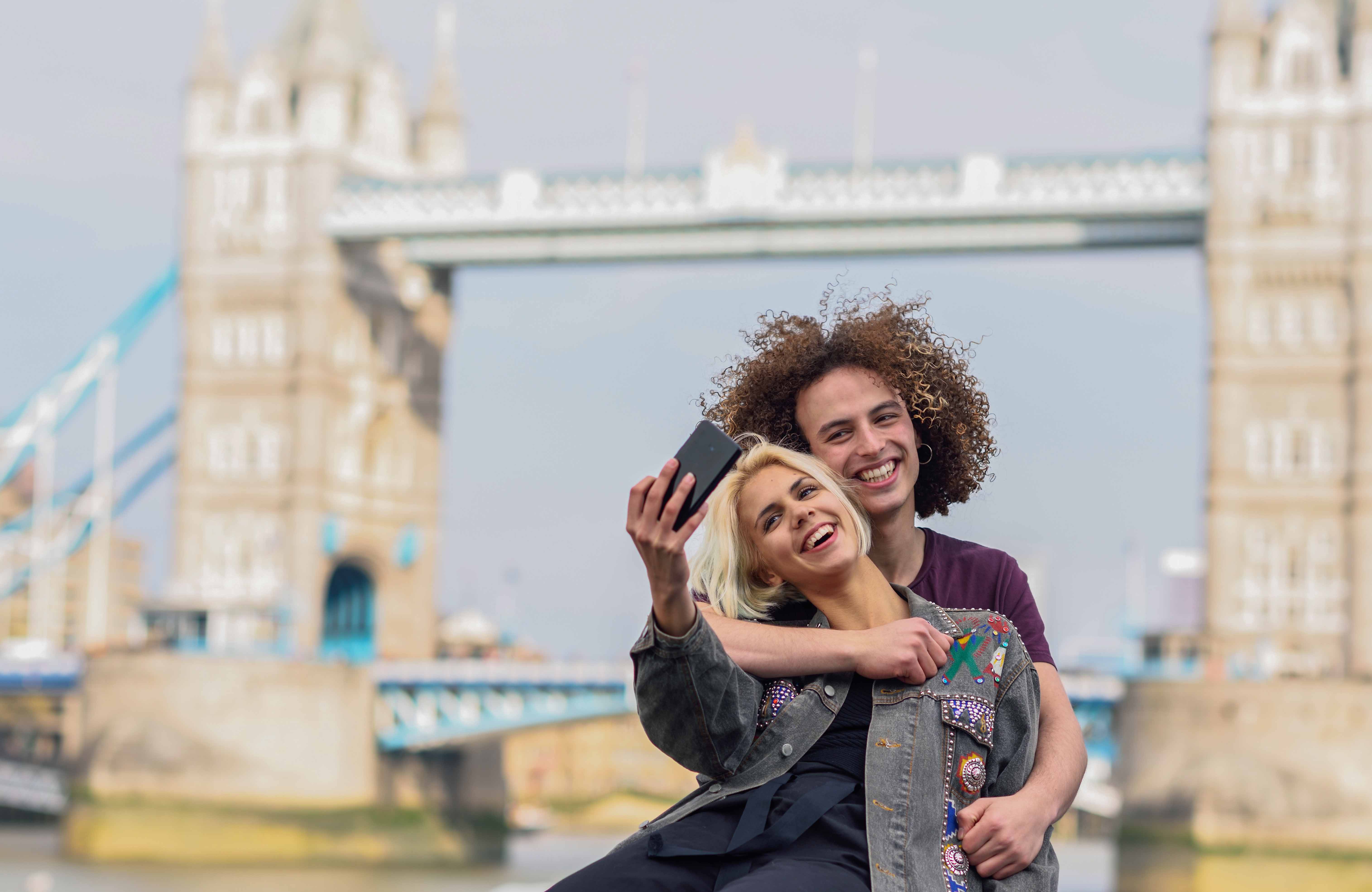 Couple taking a selfie with Tower Bridge in the background during a Thames river cruise.