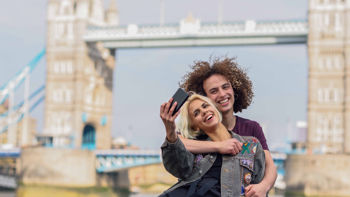 Couple taking a selfie with Tower Bridge in the background during a Thames river cruise.