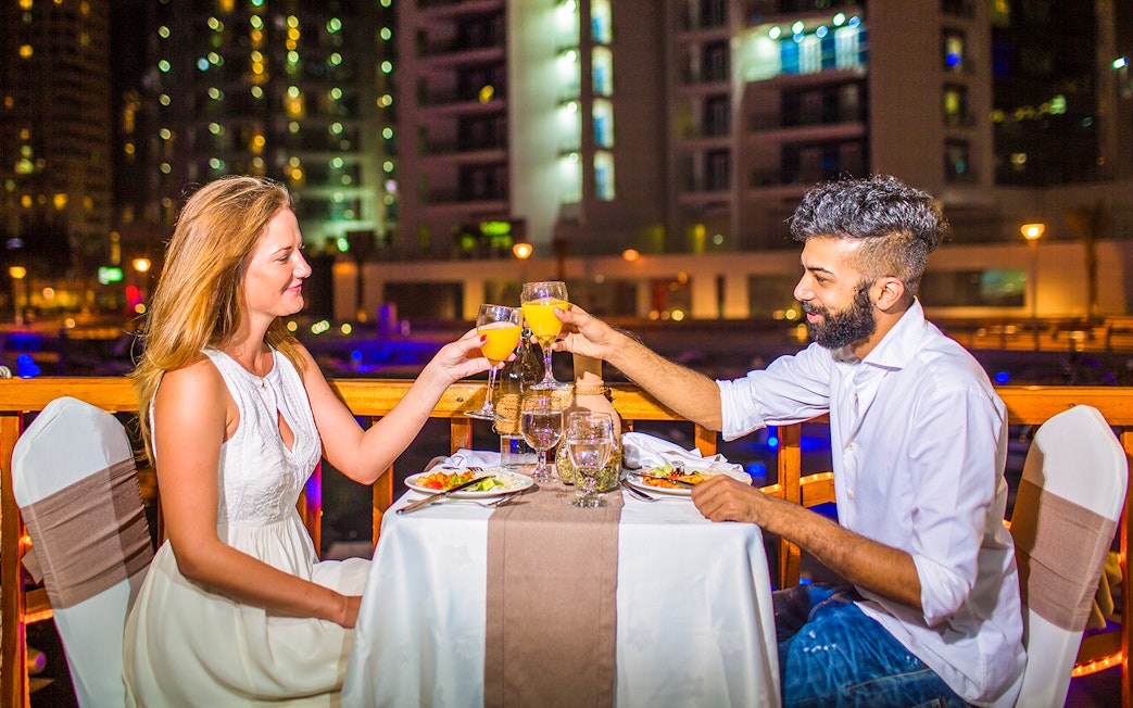Couple toasting drinks during dinner on a dhow river cruise at night.