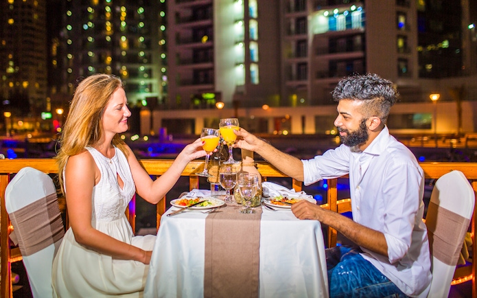 Couple toasting drinks during dinner on a dhow river cruise at night.
