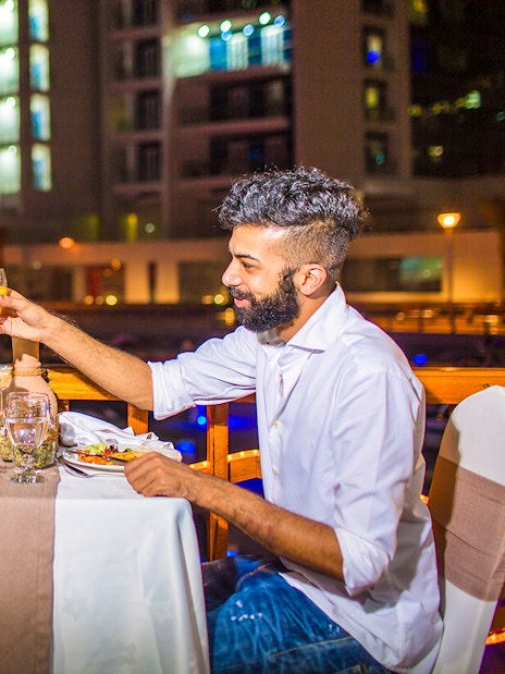 Couple toasting drinks during dinner on a dhow river cruise at night.