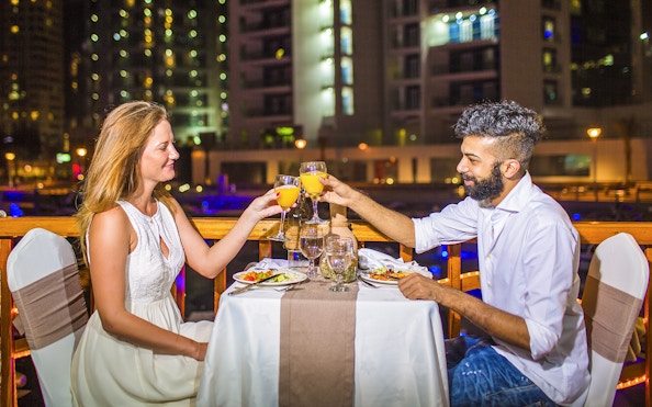Couple toasting drinks during dinner on a dhow river cruise at night.