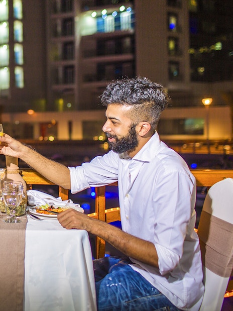 Couple toasting drinks during dinner on a dhow river cruise at night.
