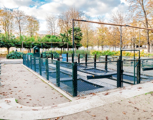 Children playing on trampolines in Tuileries Garden, Paris, with trees and historic buildings in the background.