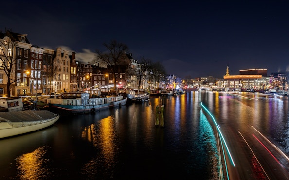 Evening view of Amsterdam canal with illuminated boats and historic buildings.