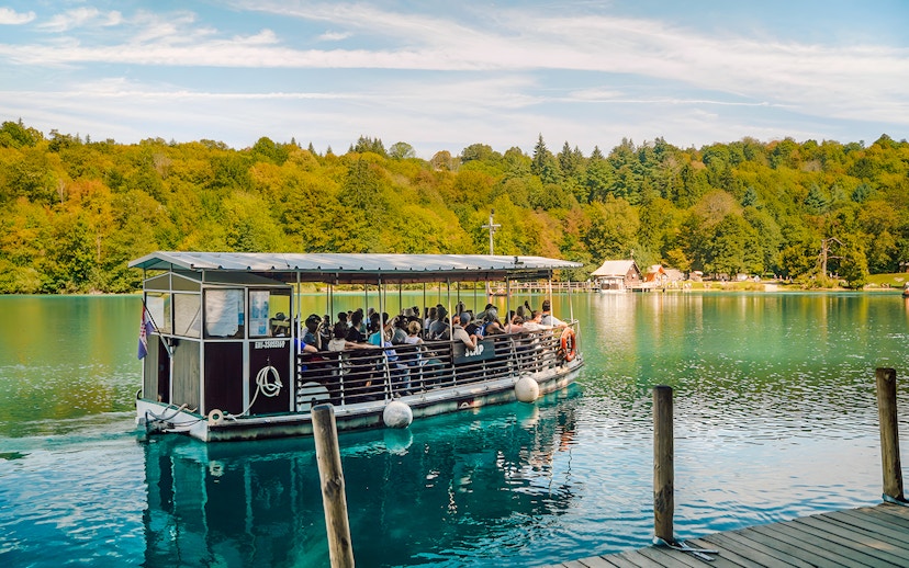 Boat tour on Plitvice Lakes with passengers enjoying scenic views of lush forests.