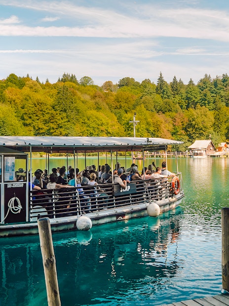 Boat tour on Plitvice Lakes with passengers enjoying scenic views of lush forests.