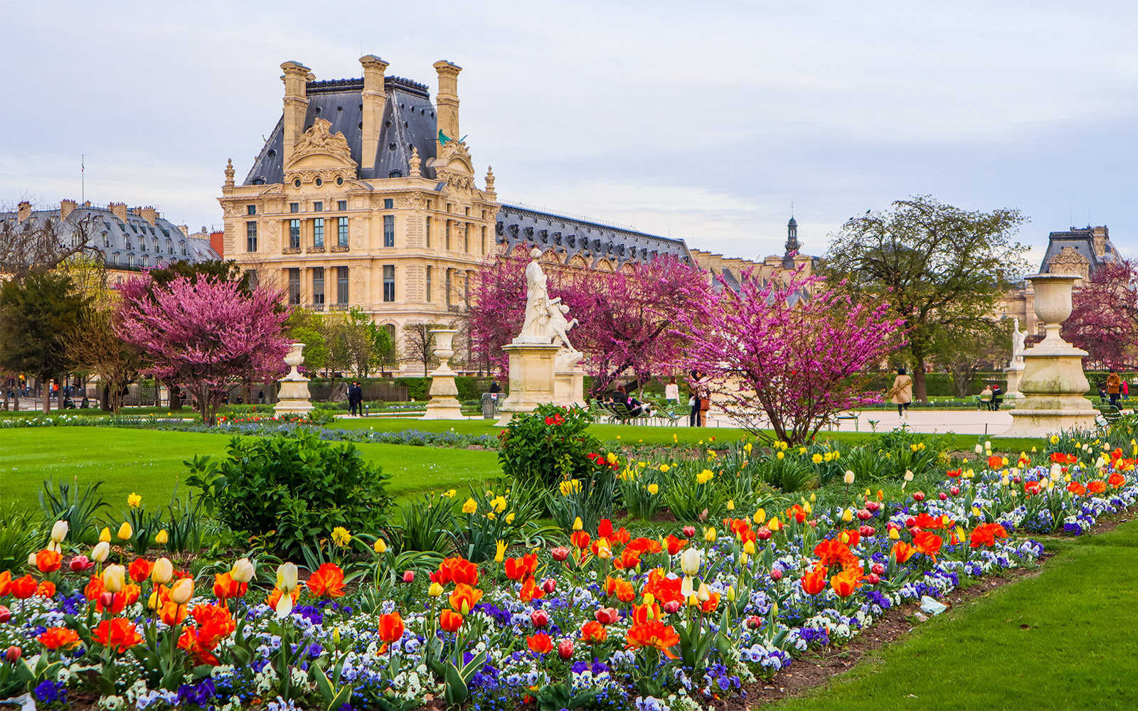 Tuileries Garden pathway with sculptures and Louvre Museum in the background, Paris.