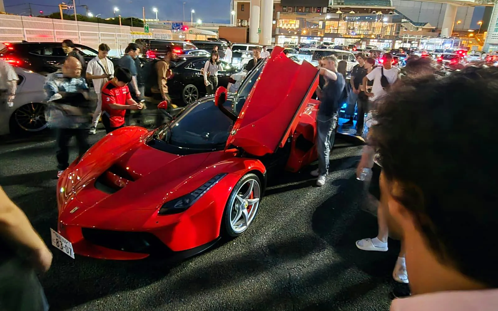 Red sports car surrounded by people during Tokyo Drift experience at night.