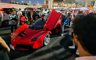 Red sports car surrounded by people during Tokyo Drift experience at night.