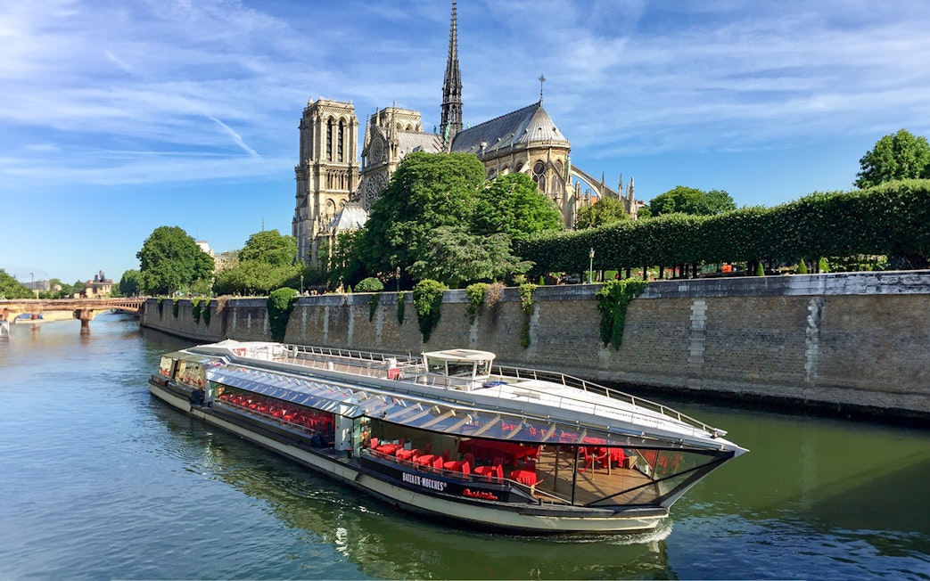 Tourists on Seine River cruise in Paris with Notre-Dame Cathedral view.