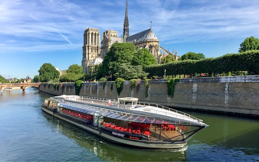 Tourists on Seine River cruise in Paris with Notre-Dame Cathedral view.