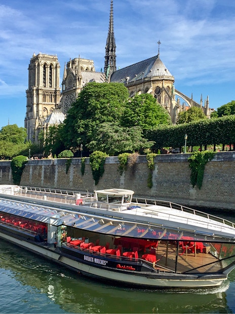 Tourists on Seine River cruise in Paris with Notre-Dame Cathedral view.