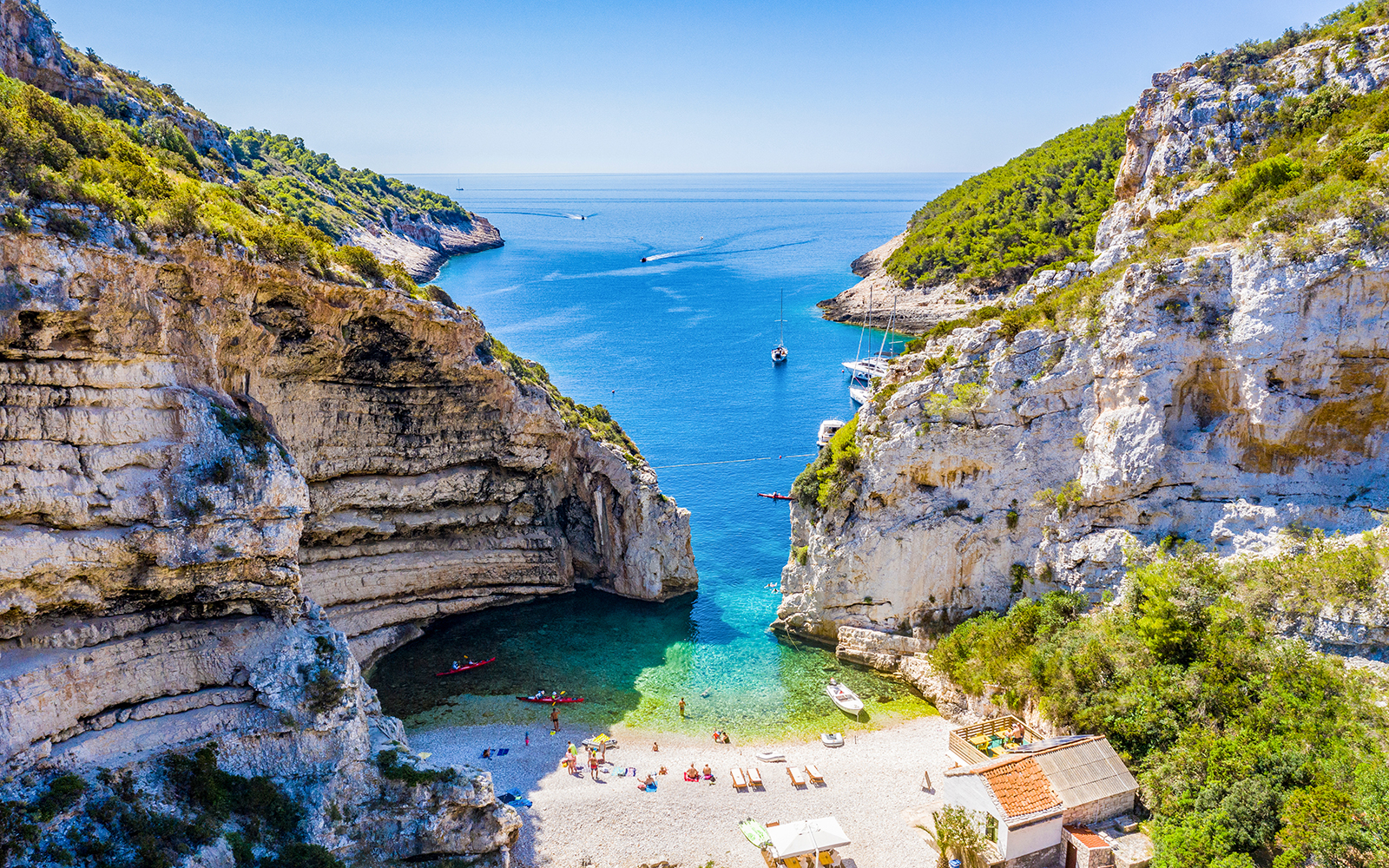 Blue Cave and Vis Island beach with boats and tourists, Croatia.