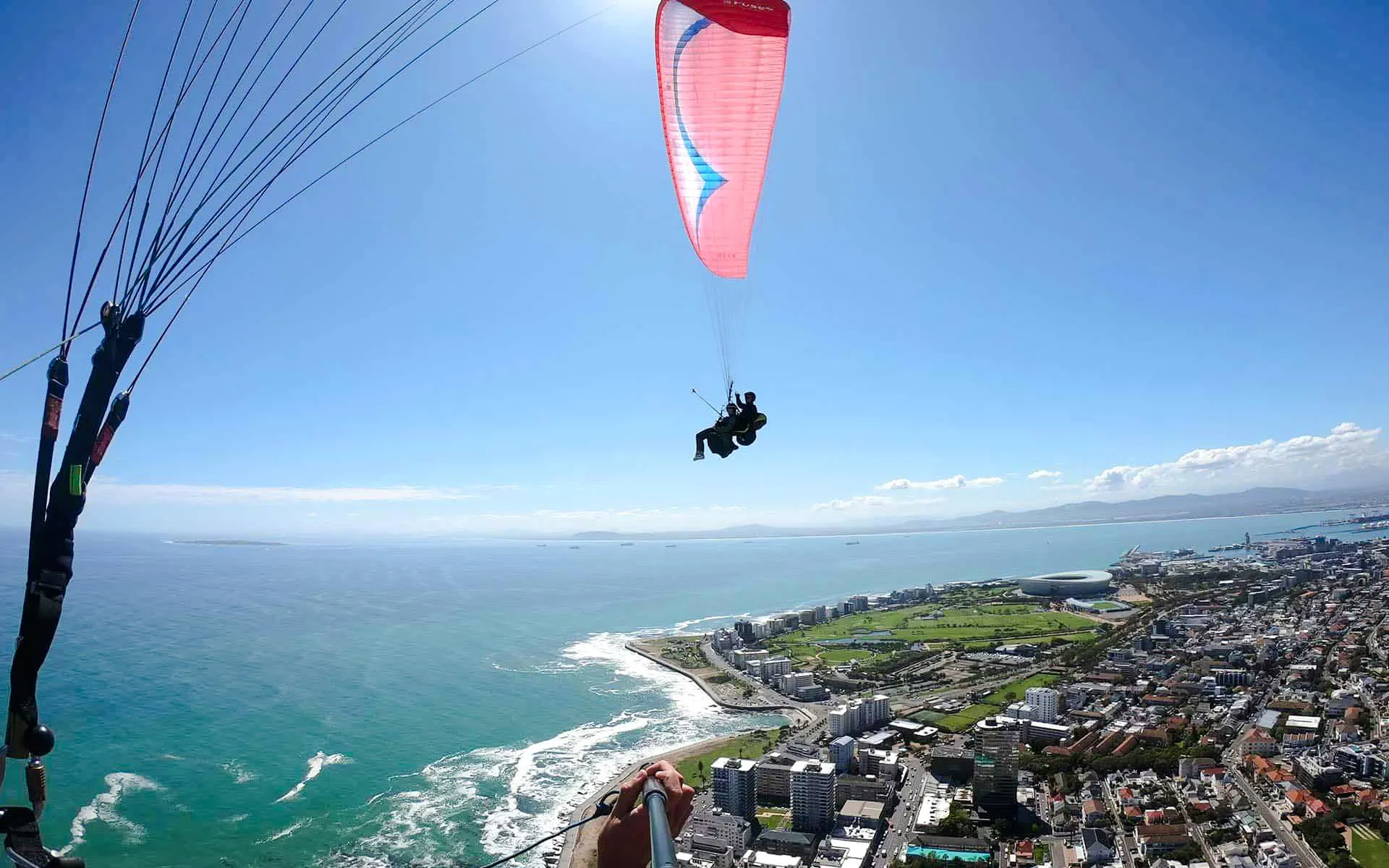 Tandem paragliding over Cape Town coastline with city and ocean views.