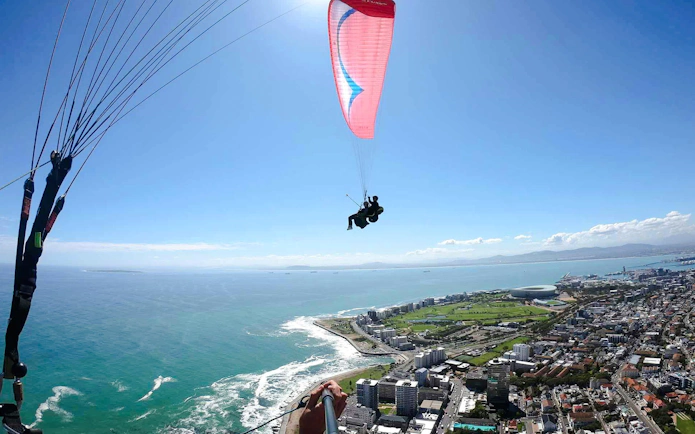 Tandem paragliding over Cape Town coastline with city and ocean views.