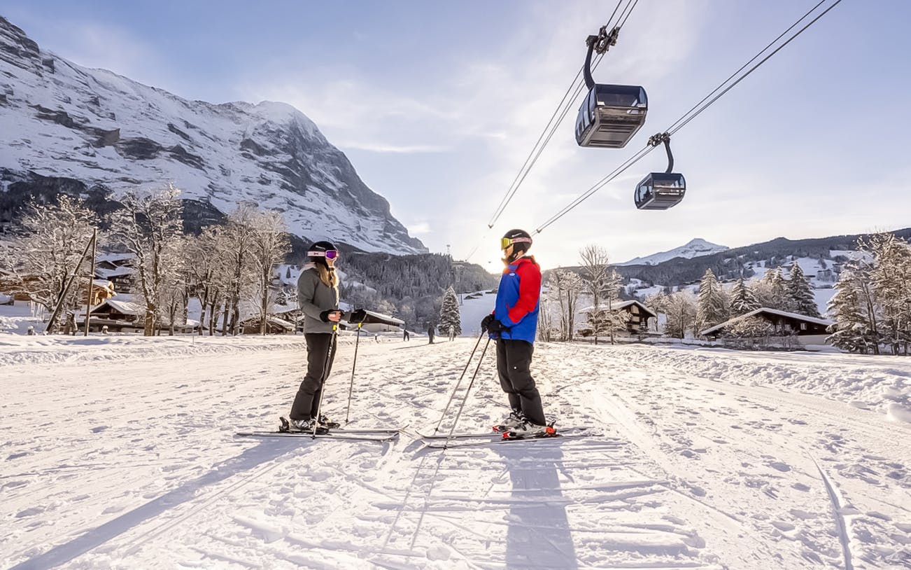 Skiers on snowy slope with Eiger Express cable cars in Grindelwald, Switzerland.