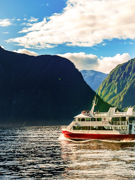 Cruise boat on Milford Sound with towering cliffs, Southern Discoveries tour.