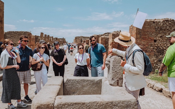 Visitors on a guided tour in Pompeii, exploring ancient ruins with a guide.