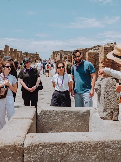 Visitors on a guided tour in Pompeii, exploring ancient ruins with a guide.