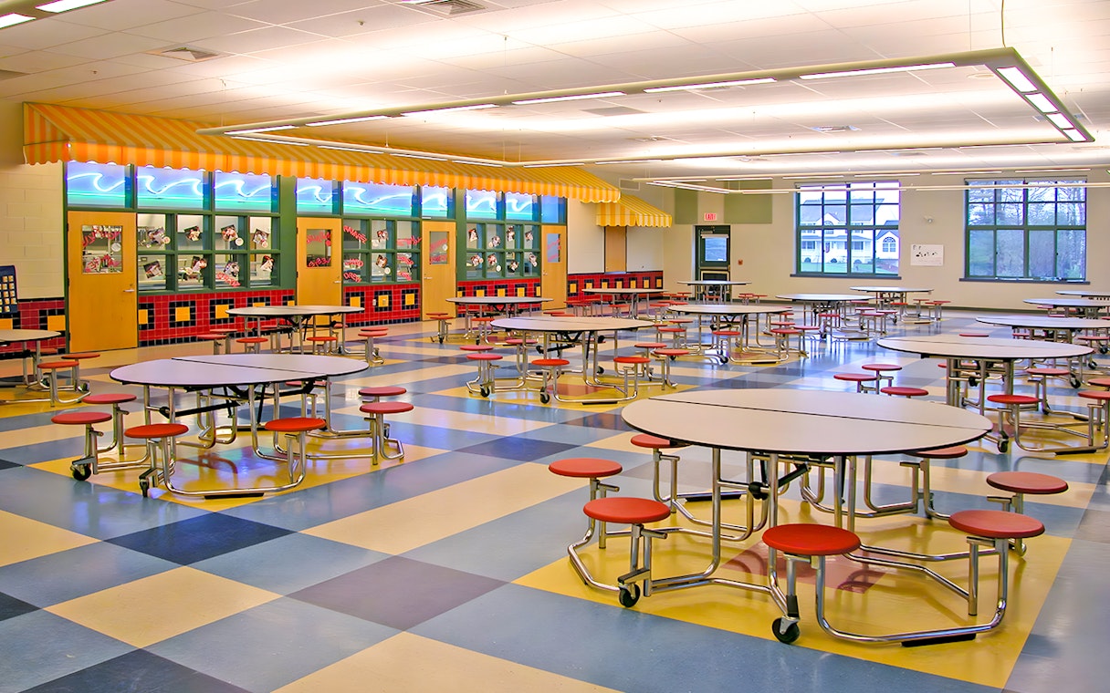 Colorful cafeteria with round tables and red stools at KidsSTOP Singapore.