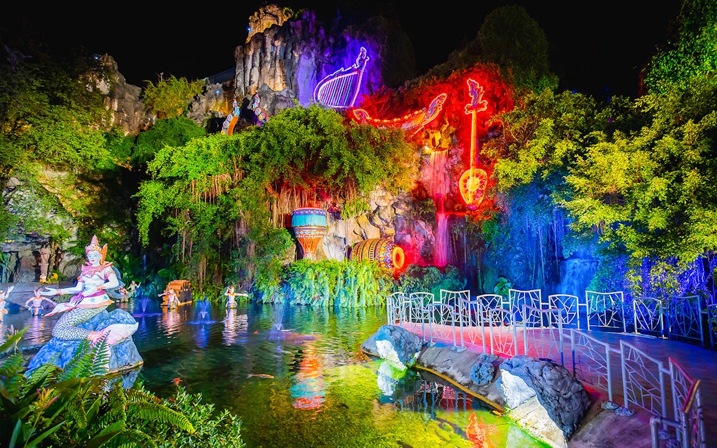 Phuket Fantasea night show with neon lights and mythical statues by a pond.