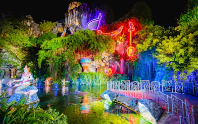 Phuket Fantasea night show with neon lights and mythical statues by a pond.