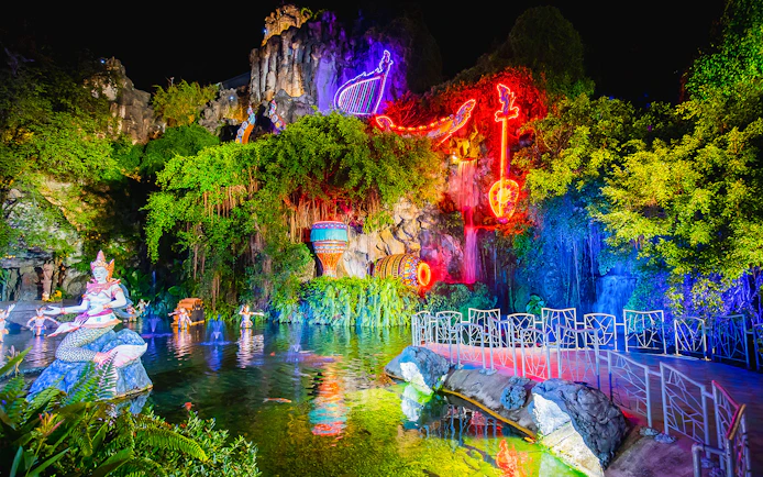 Phuket Fantasea night show with neon lights and mythical statues by a pond.