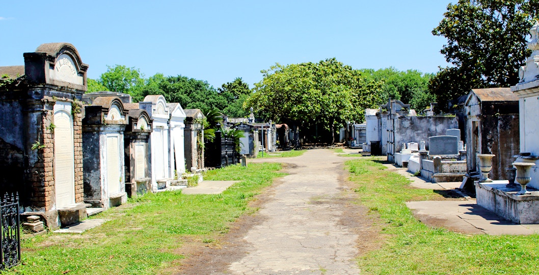 Above-ground tombs in a New Orleans cemetery, Louisiana, with a tree-lined path.