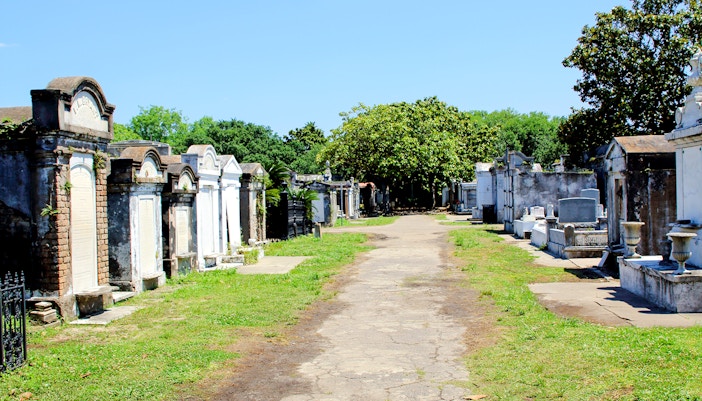 Above-ground tombs in a New Orleans cemetery, Louisiana, with a tree-lined path.