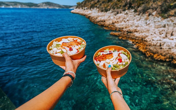 Bowls of salad held over clear blue water on a catamaran cruise near Hvar and Pakleni Islands.