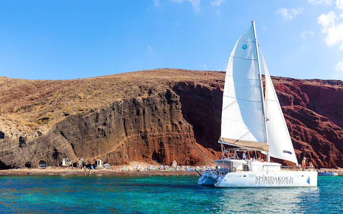 Catamaran sailing near the cliffs of Santorini on the Joy Daytime Cruise.
