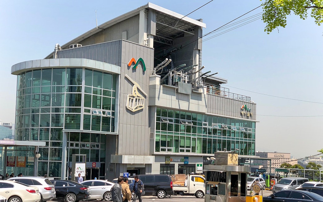 Entrance of cable car station in Namsan, Seoul, with parked cars in front.