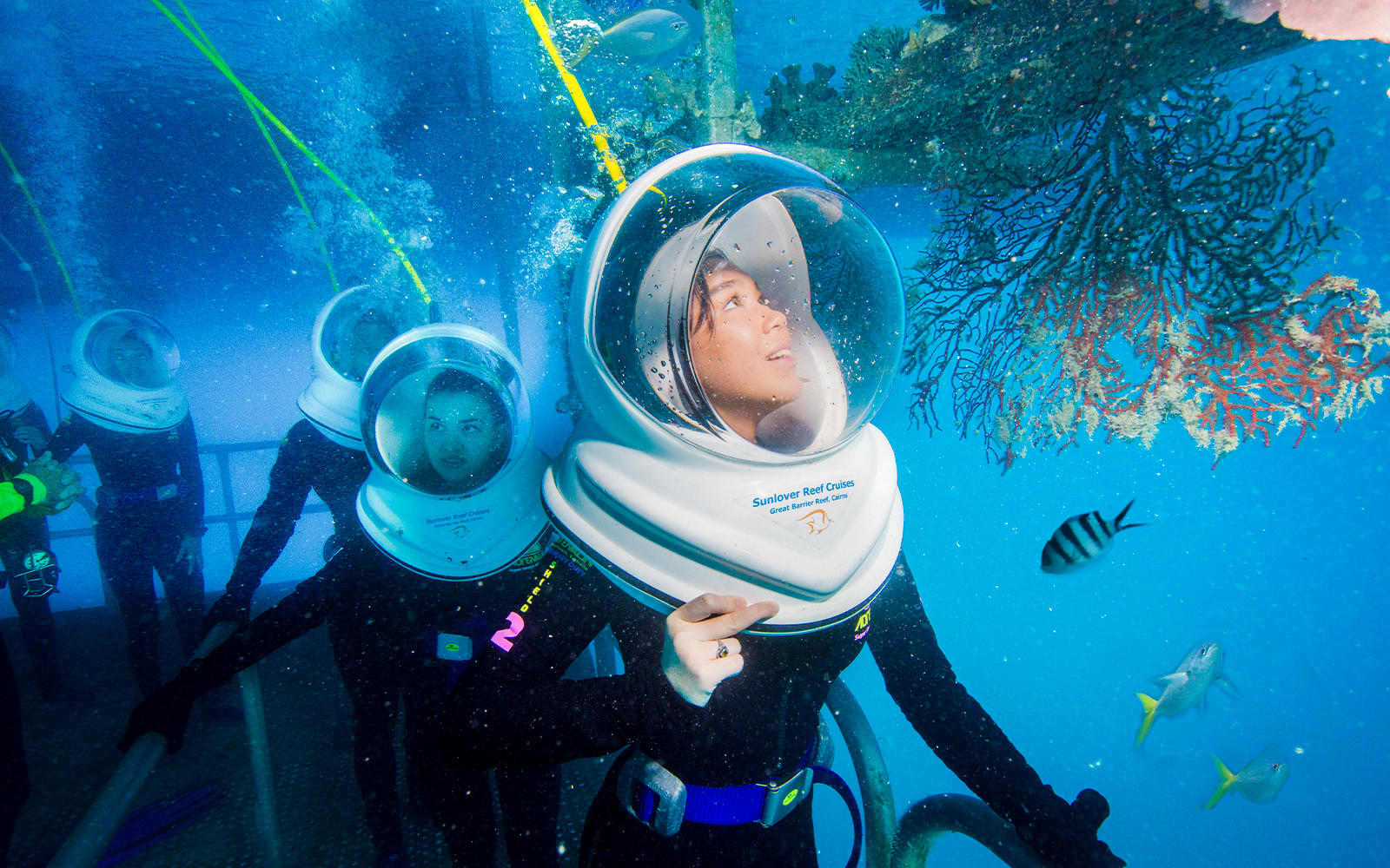 Tourists on Seawalker helmet dive at Moore Reef, Great Barrier Reef, observing coral and fish.