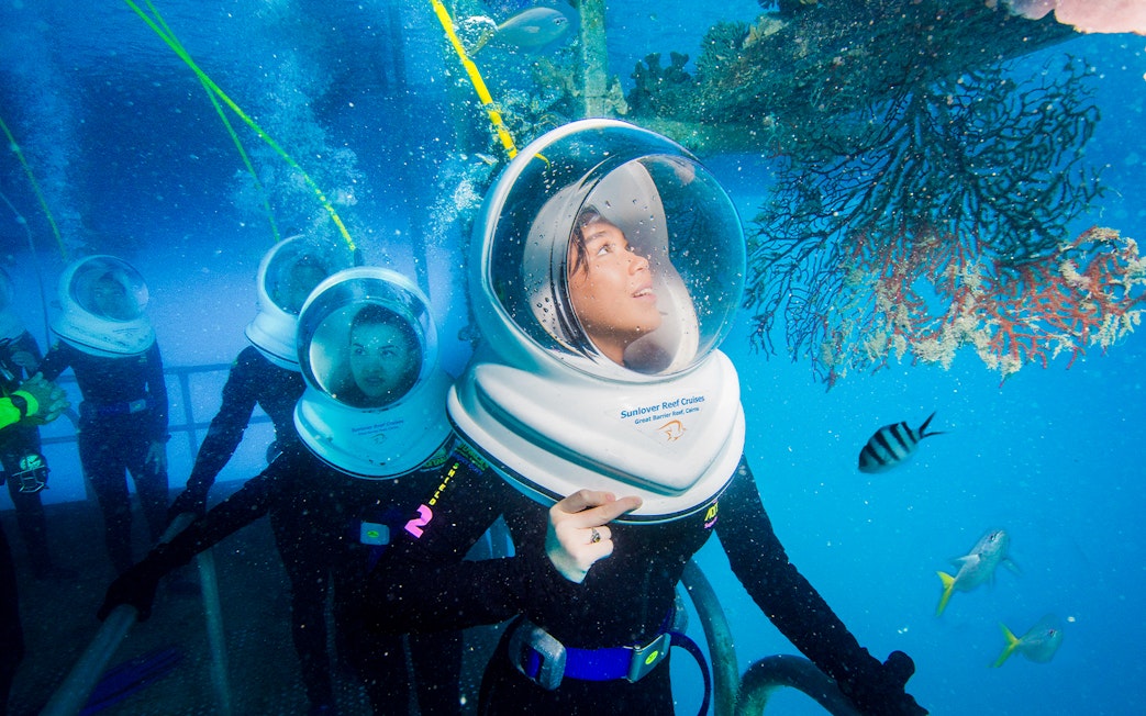 Tourists on Seawalker helmet dive at Moore Reef, Great Barrier Reef, observing coral and fish.