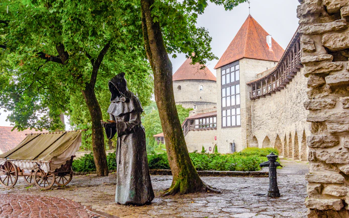 Statue of a monk near medieval towers in Danish King’s Garden, Tallinn, Estonia, on a rainy day.