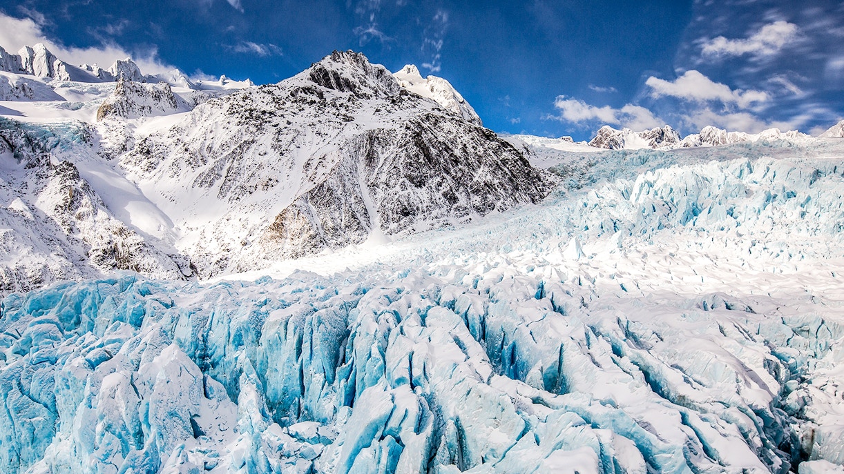 Franz Josef Glacier aerial view, showcasing icy crevasses and snow-covered peaks in New Zealand.