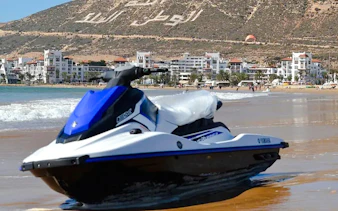 Jet ski on Agadir beach with cityscape and hillside in background.