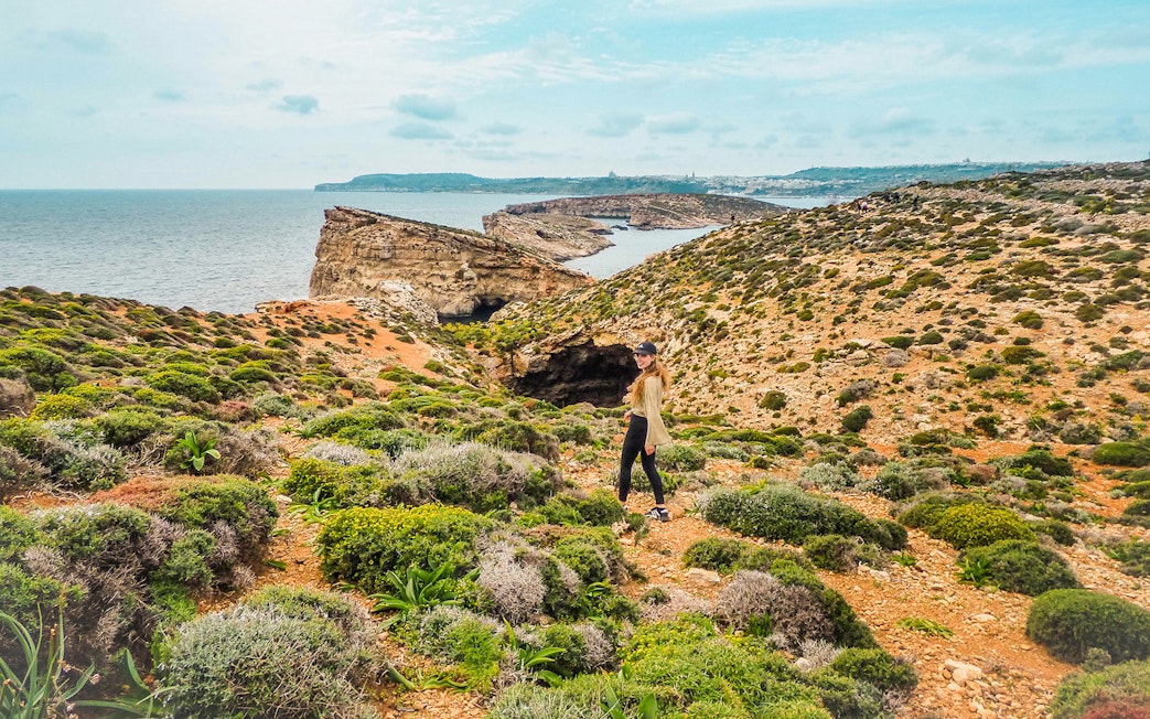 Lady walking on Comino Island with coastal cliffs in the background.