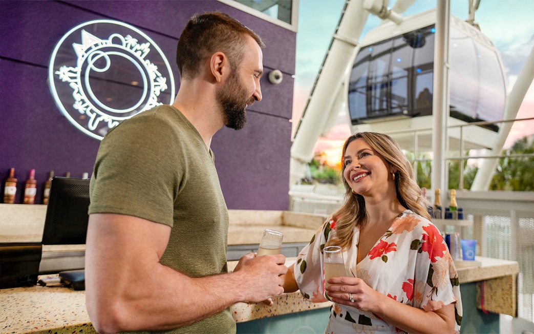 Couple enjoying drinks at ICON Park, Orlando with Ferris wheel in background.