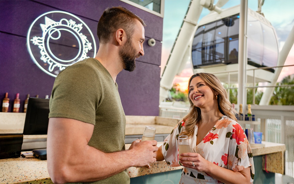 Couple enjoying drinks at ICON Park, Orlando with Ferris wheel in background.
