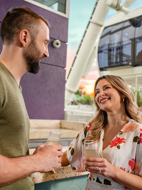 Couple enjoying drinks at ICON Park, Orlando with Ferris wheel in background.