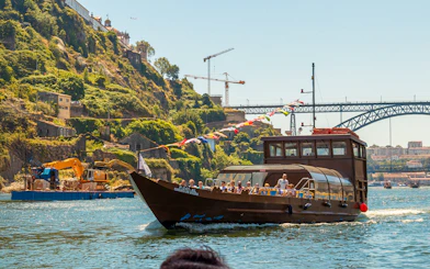 Tourists on a Douro River cruise boat with scenic hillside and bridge in Porto, Portugal.