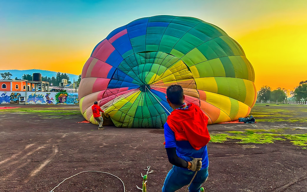 Preparing a colorful hot air balloon for flight at sunrise in Teotihuacan, Mexico.