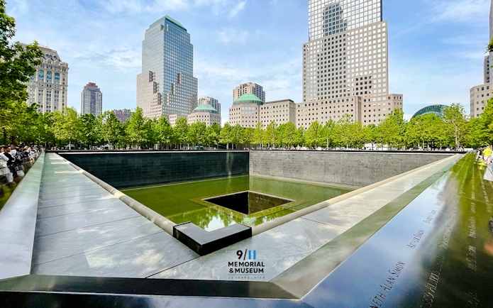 Reflecting pool at 9/11 Memorial in New York City with surrounding skyscrapers.