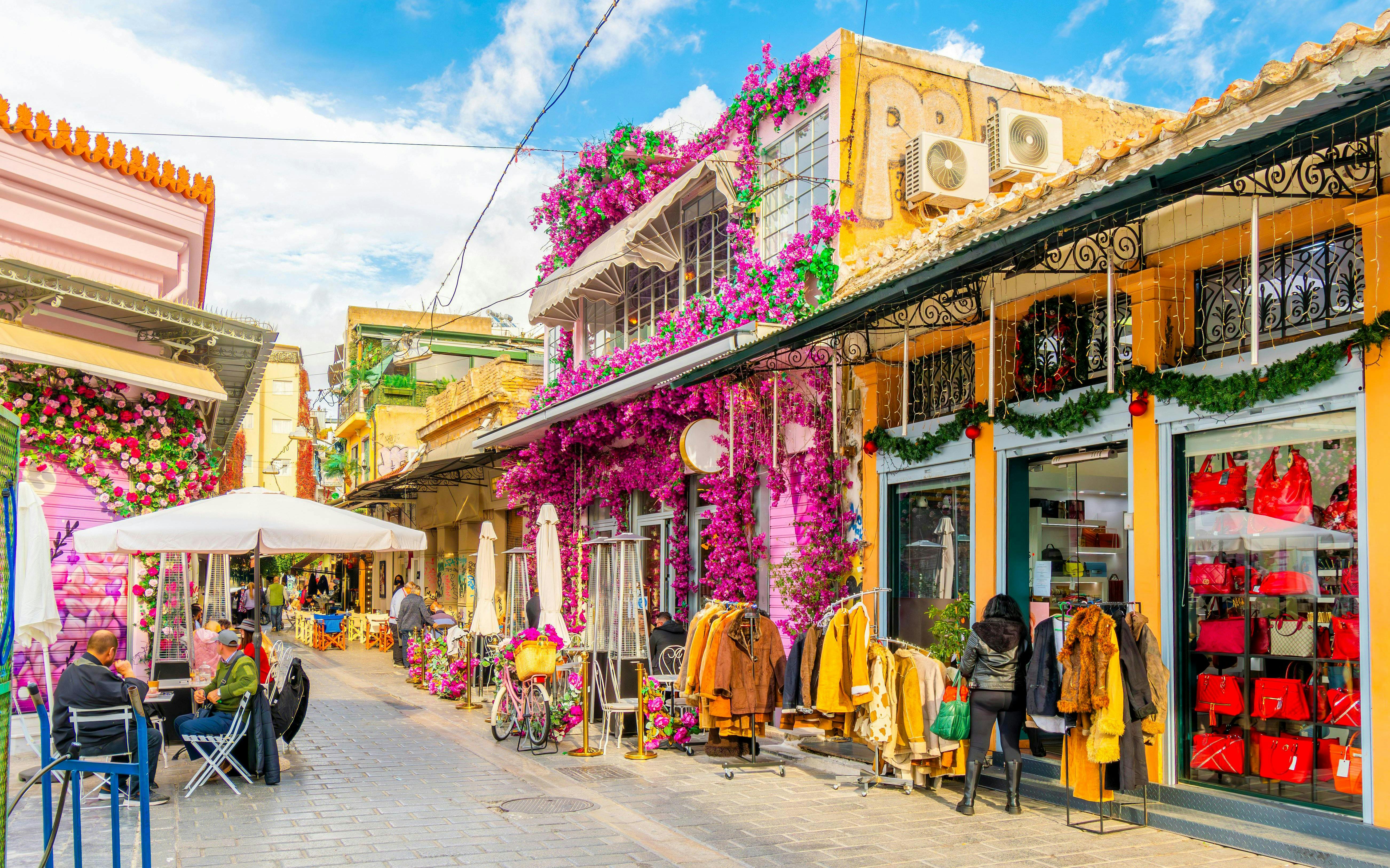 Shops and cafes in a vibrant street near Plaka, Athens, Greece, with colorful flowers and clothing displays.
